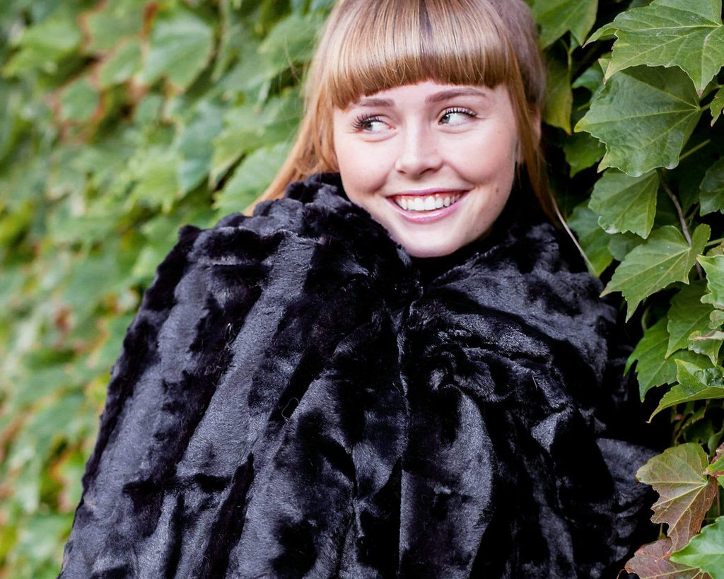Young woman cuddled up in a black minky blanket standing against an ivy covered wall.