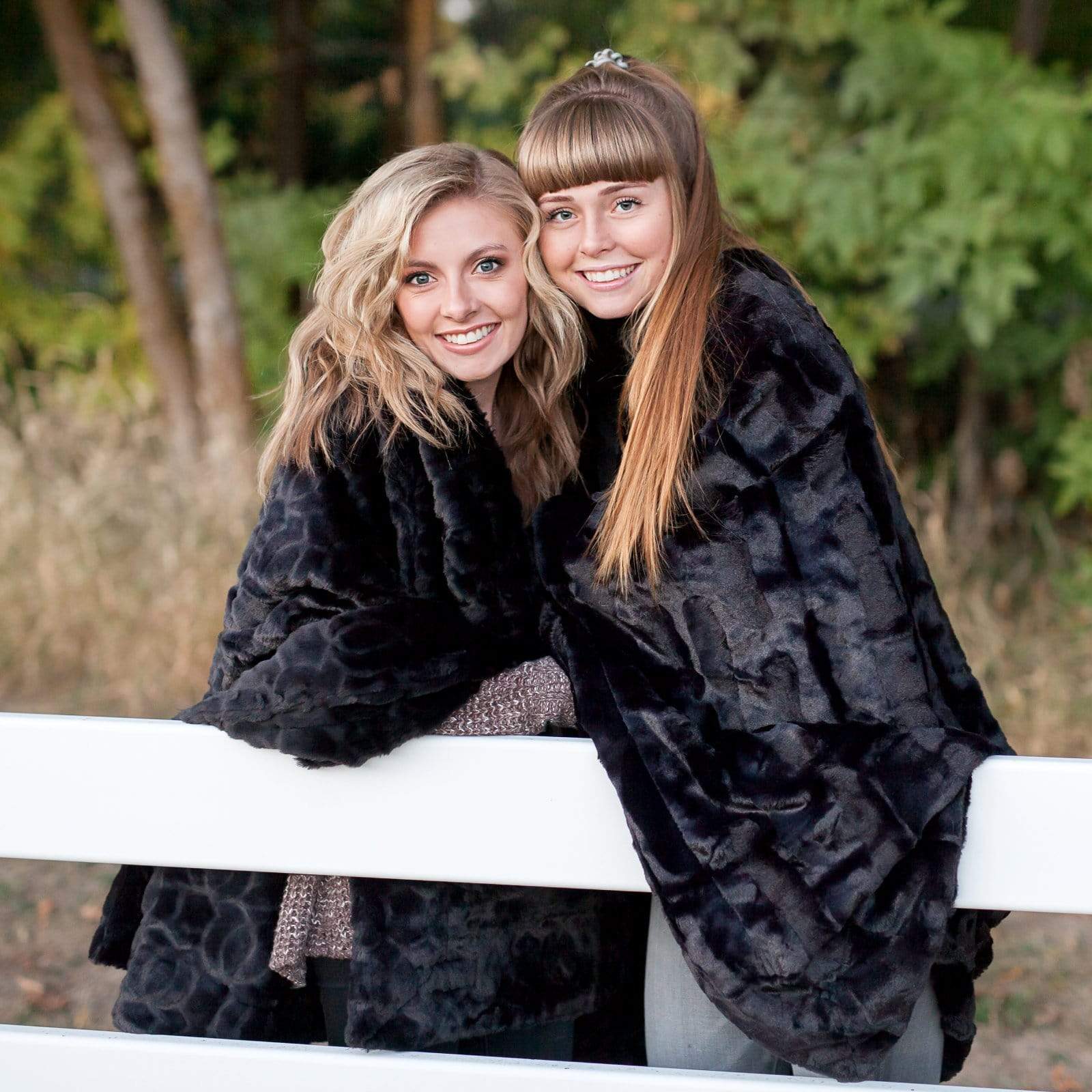 Two young women wrapped in black minky couture blankets. 