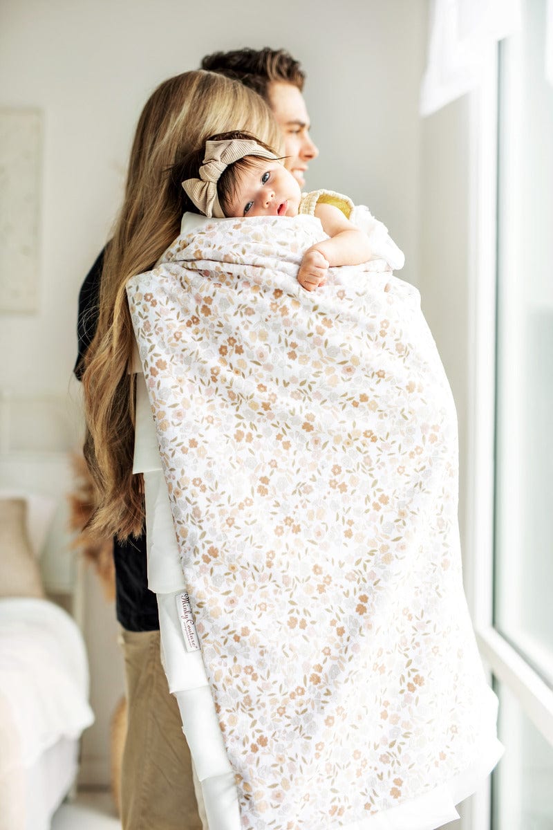 Baby girl laying on her moms shoulder wrapped in a blanket with a small floral blanket. 