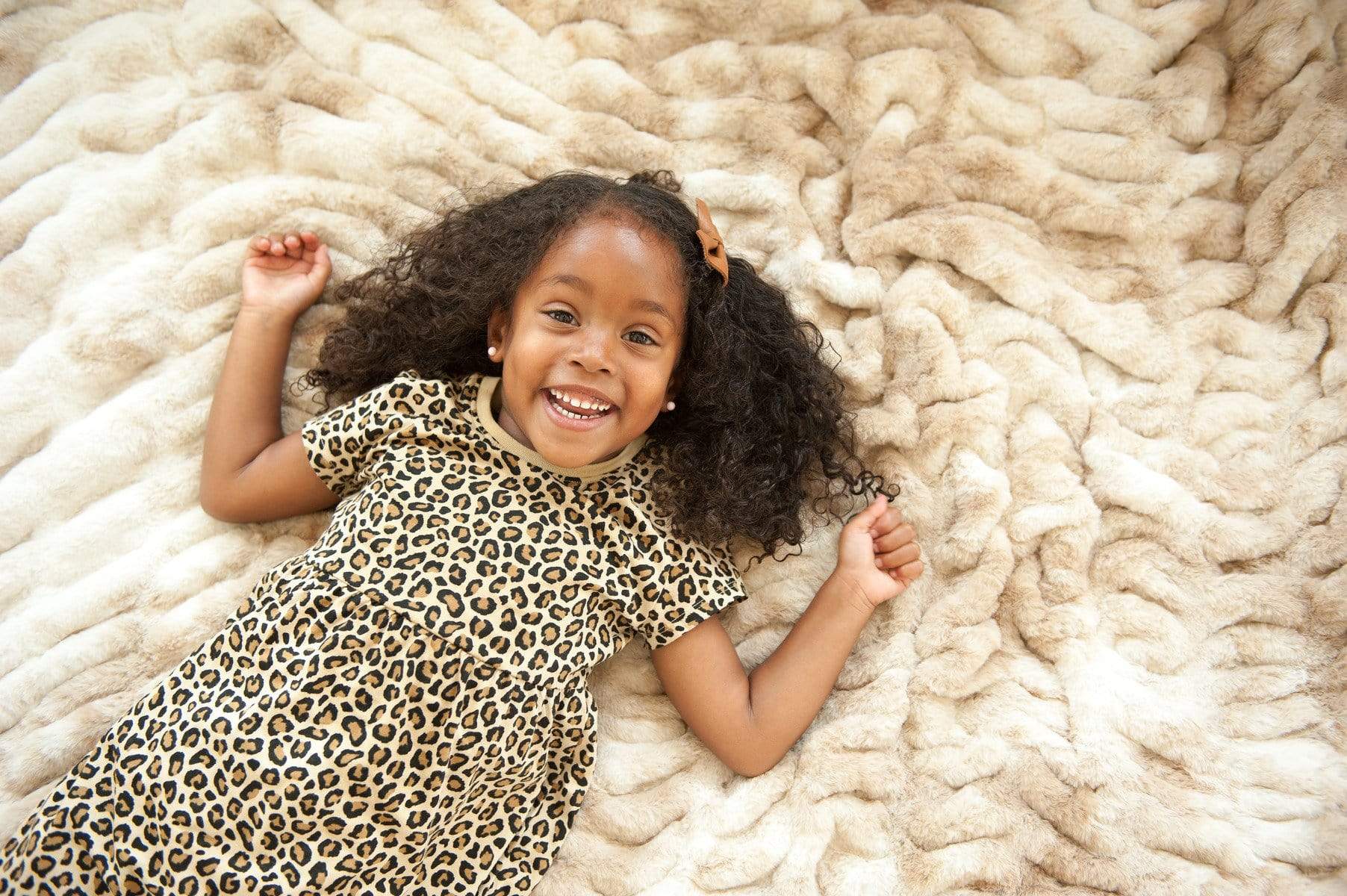Little girl laying on top of the cozy cotton candy caramel hugs stretchy blanket by Minky Couture.
