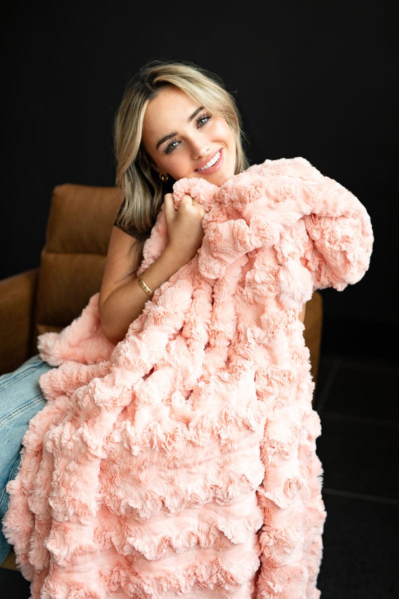 Young girl sitting on a brown leather chair while holding a soft pink colored blanket.