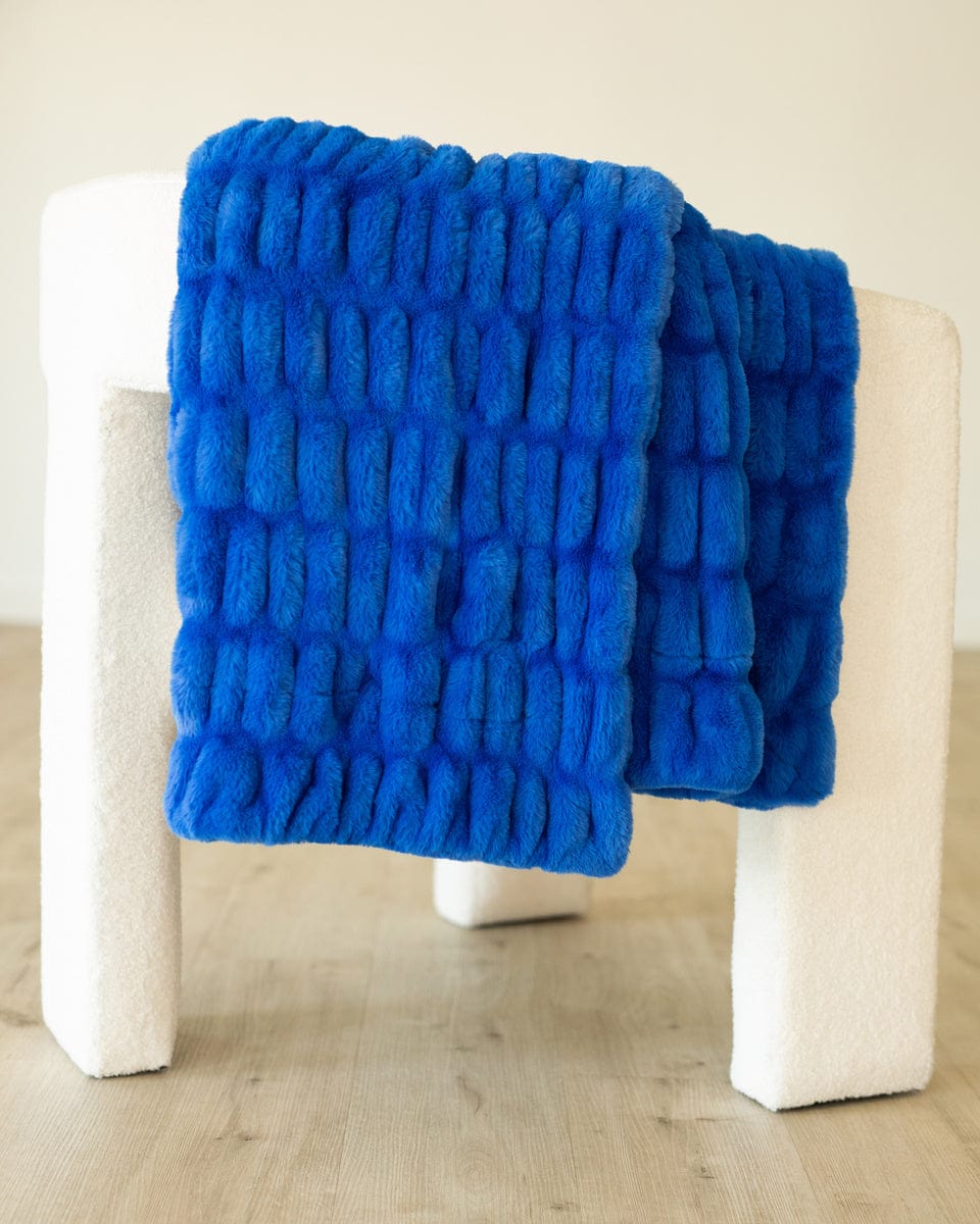 Stretchy blue plush blanket handing over the side of a white chair.