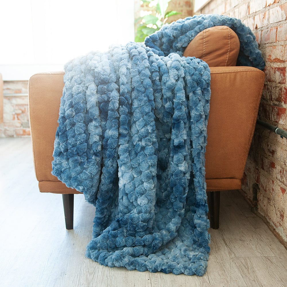Blue waffle textured blanket draped over a brown leather couch.