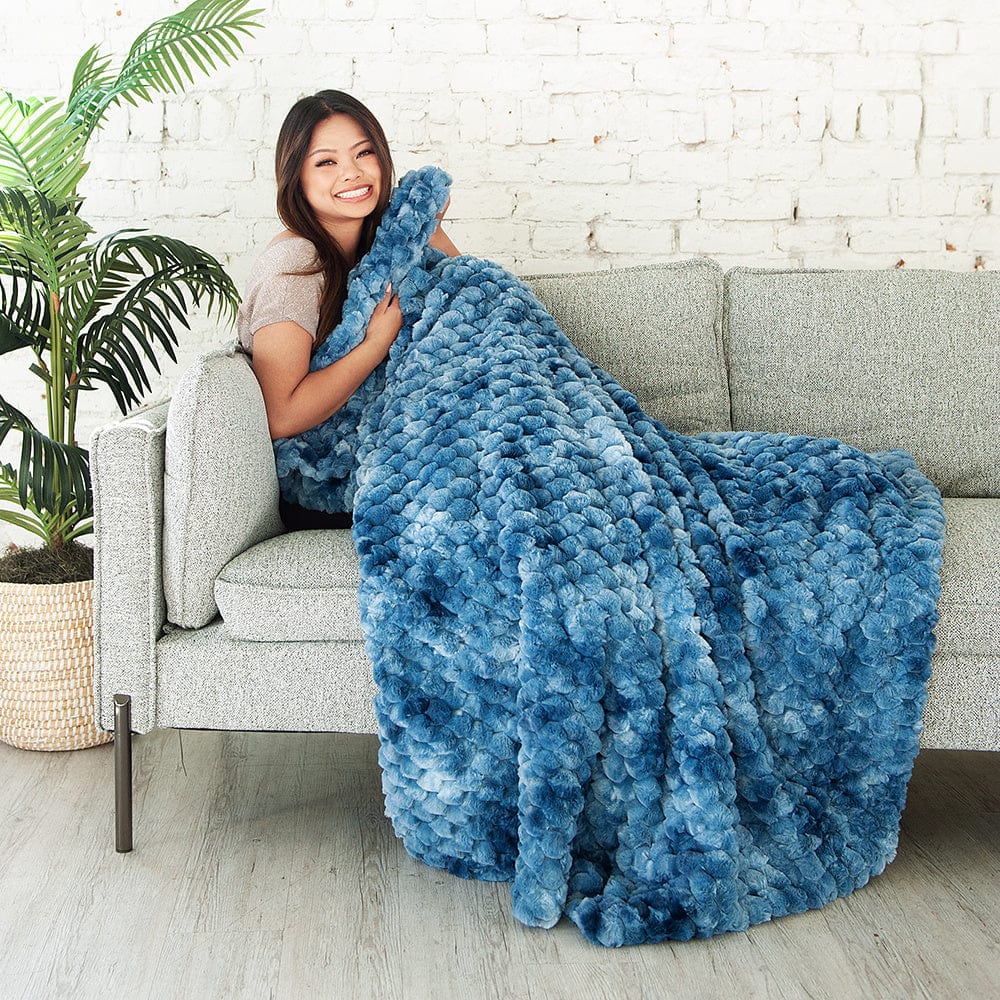 Woman sitting on a gray couch while wrapped in a bright blue waffle textured blanket.