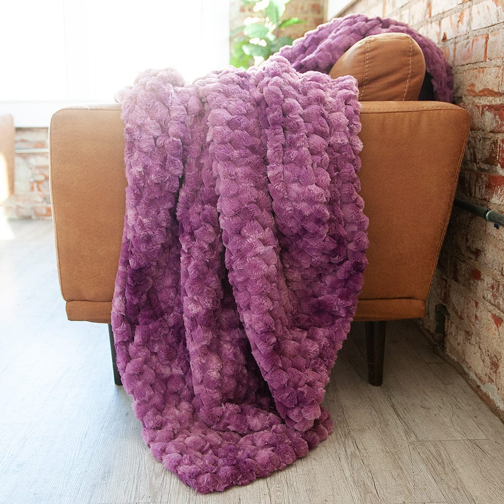 Purple waffle textured blanket draped over the side of a brown leather couch.