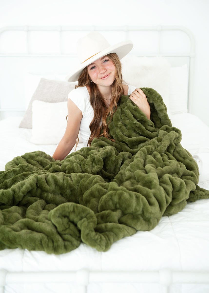 Young woman sitting on a bed with a dark olive plush blanket