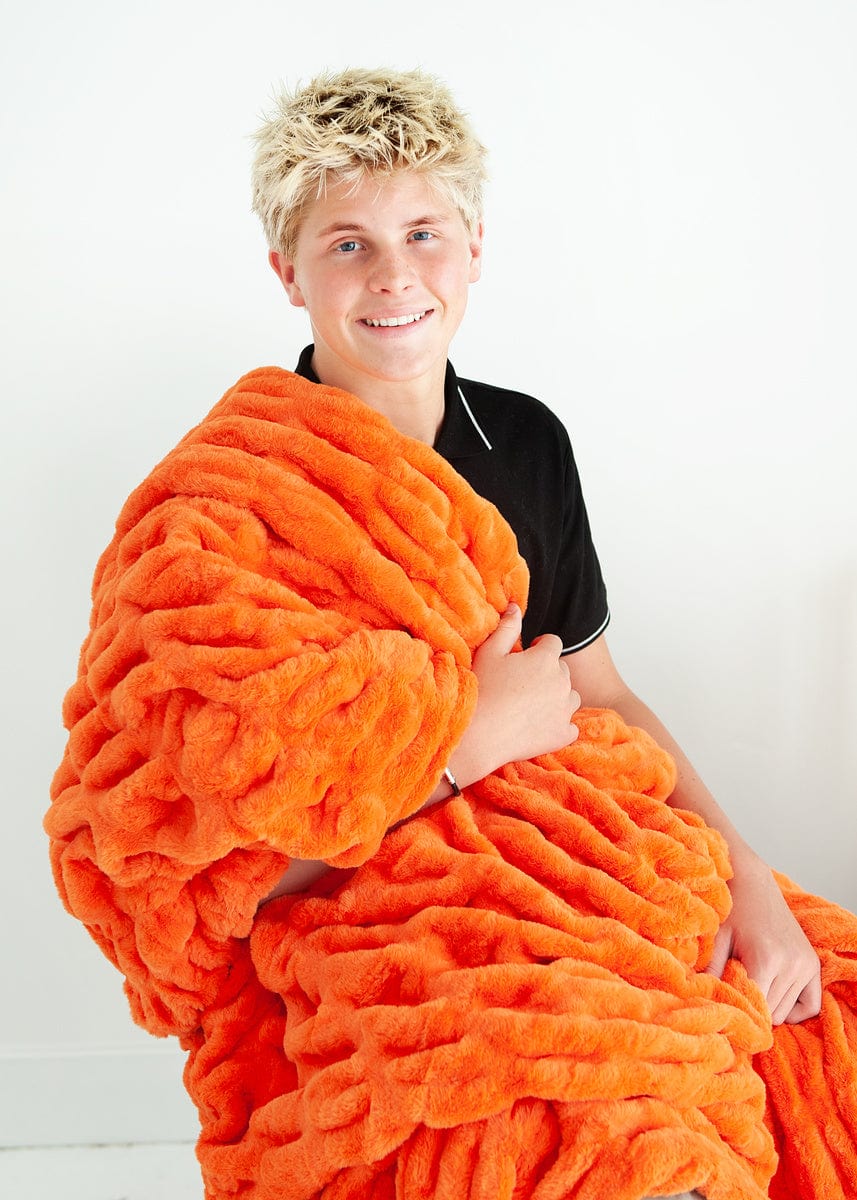 Young man sitting with a vibrant orange ruched blanket over one shoulder.