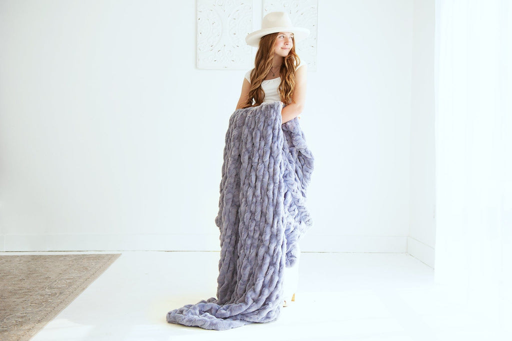 Young woman holding a light purple blanket over her arms as she stands. 