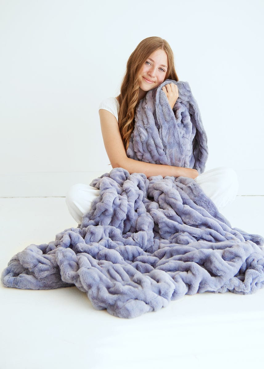 Young woman sitting with a grayish purple ruched plush blanket. 