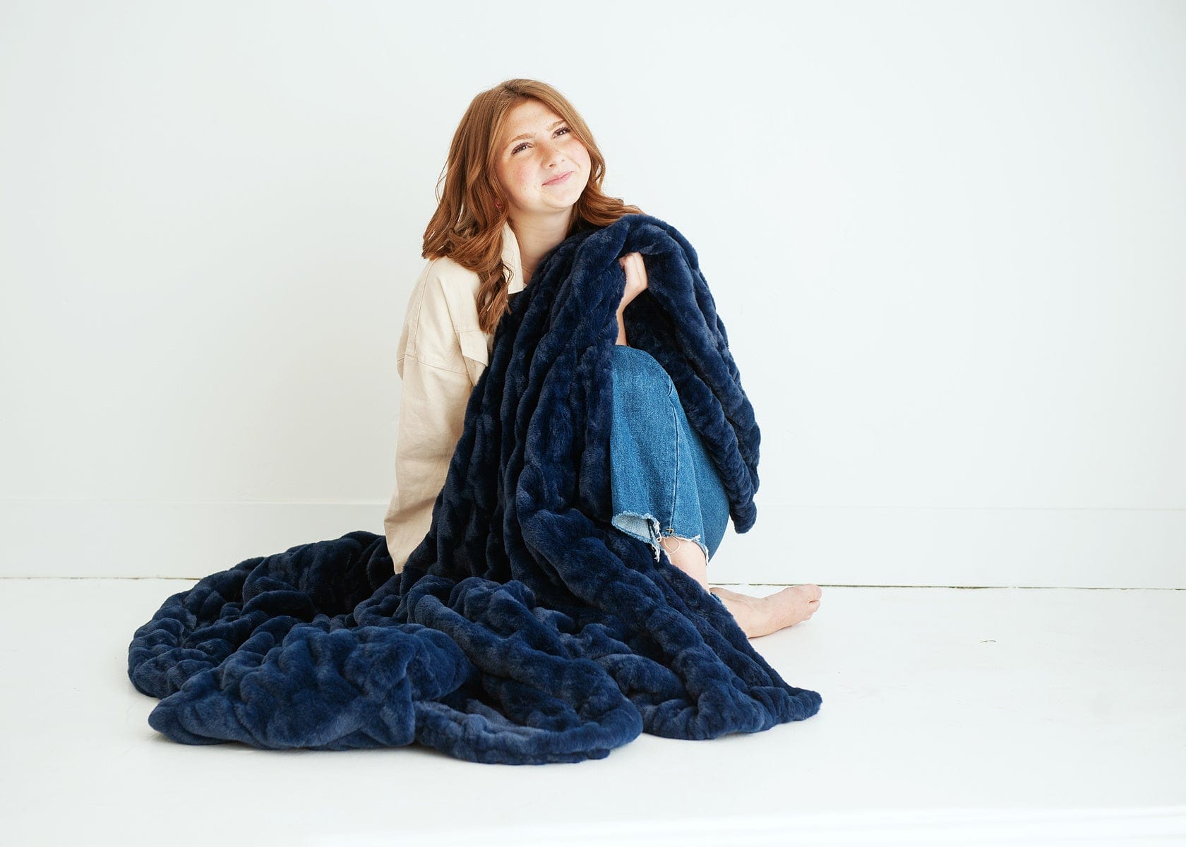 Young woman sitting on the ground holding a navy blue plush blanket.