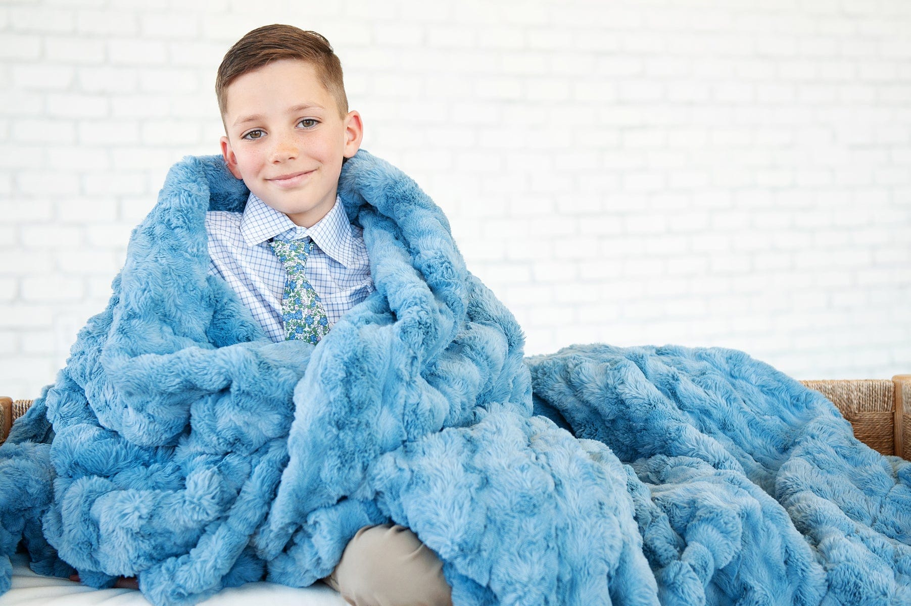 Young boy sitting while wrapped up in a faded denim blue colored blanket.