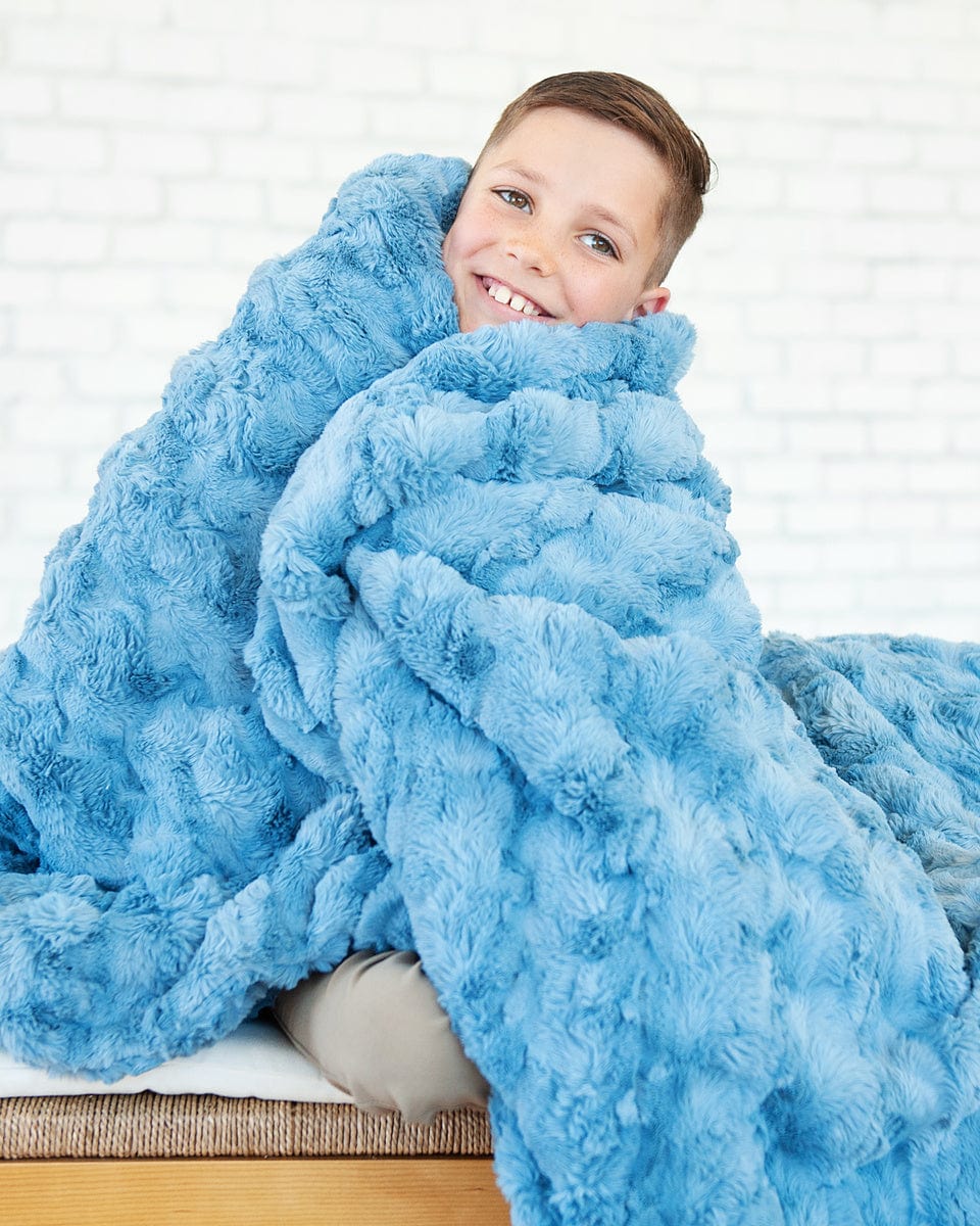 Young boy snuggling up in a faded denim blue colored blanket.