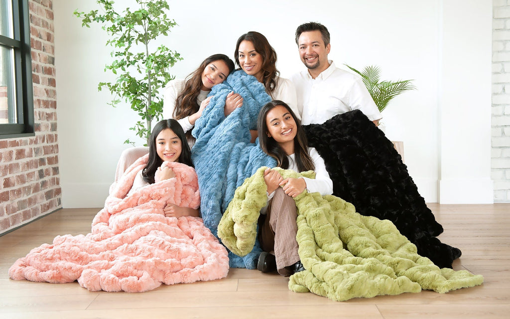 Young family sitting together wrapped up in four different colored blankets.