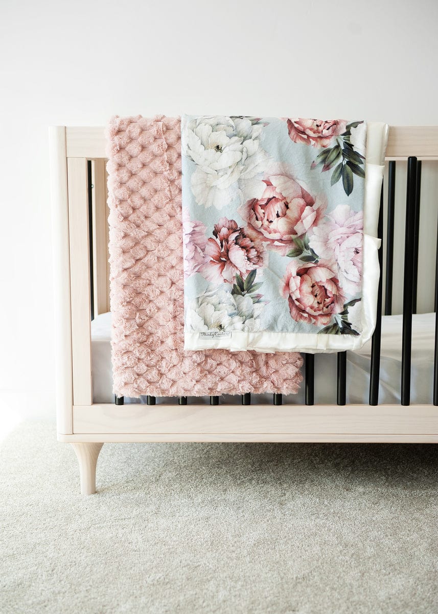 Blush waffle textured blanket and a blush and cream floral peony patterned blanket hanging over the side of a crib.