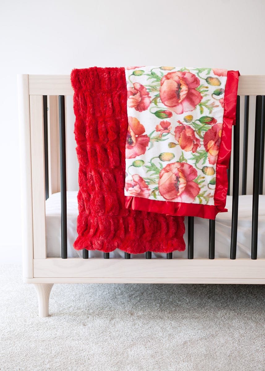 Red ruched blanket and a red poppy patterned blanket hanging over the side of a crib.