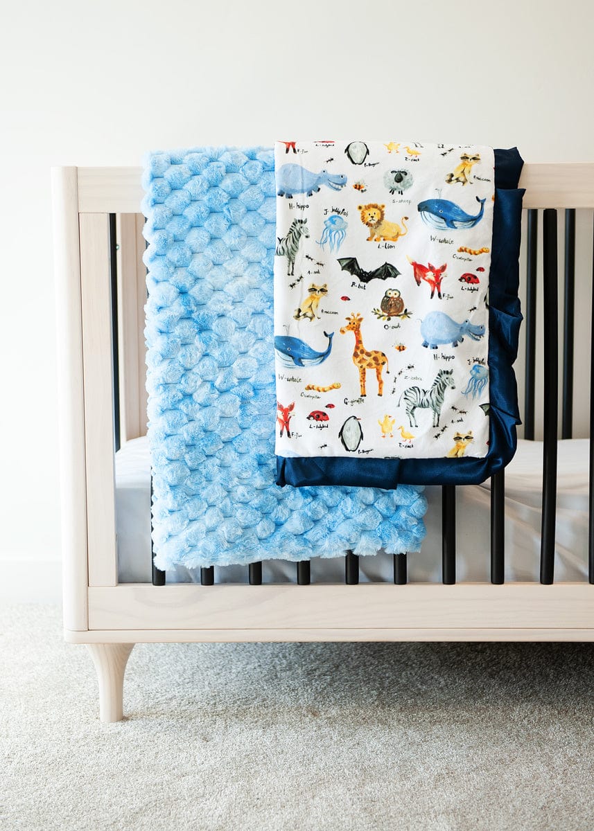 Light blue waffle textured blanket and a zoo animal themed blanket laying over the side of a crib. 