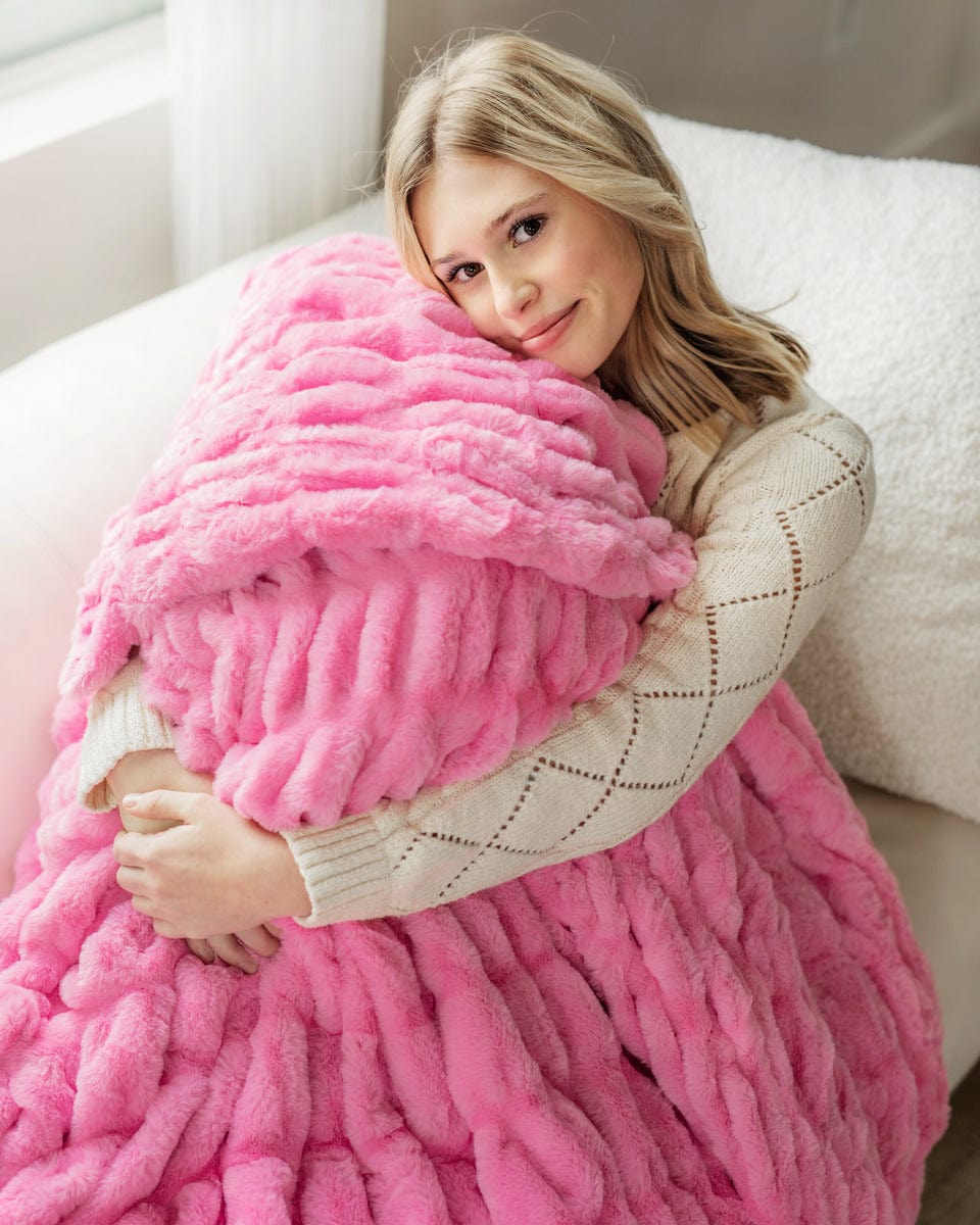 Young woman sitting with her knees pulled up covered in a hot pink ruched plush blanket.