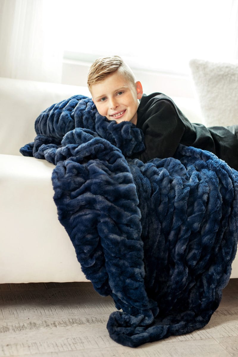 Little boy laying on a couch hugging a navy blue plush blanket. 