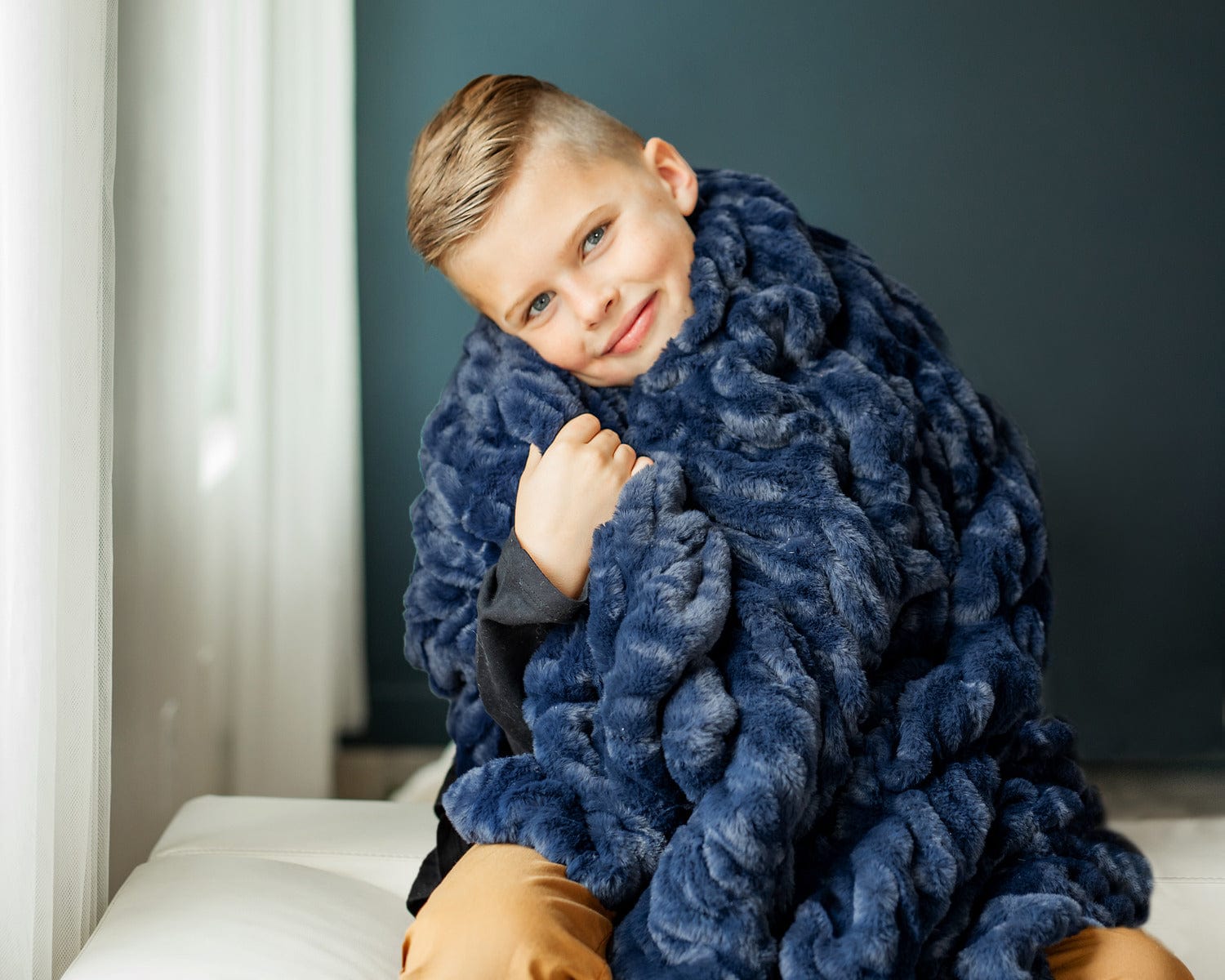 Little boy with a navy blue plush blanket wrapped around his shoulders.