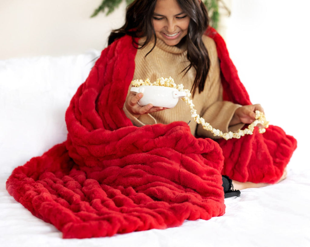 Young woman making a popcorn garland while wrapped up in a red ruched plush blanket. 