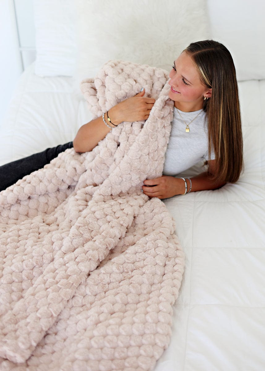 Women snuggling up on a white bed with a light tan waffle textured blanket.
