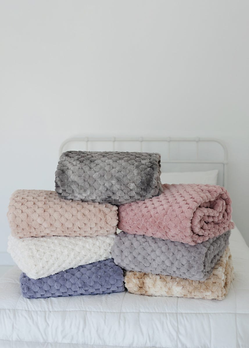 Seven varying colored waffle textured blankets folded neatly on a white bed comforter.