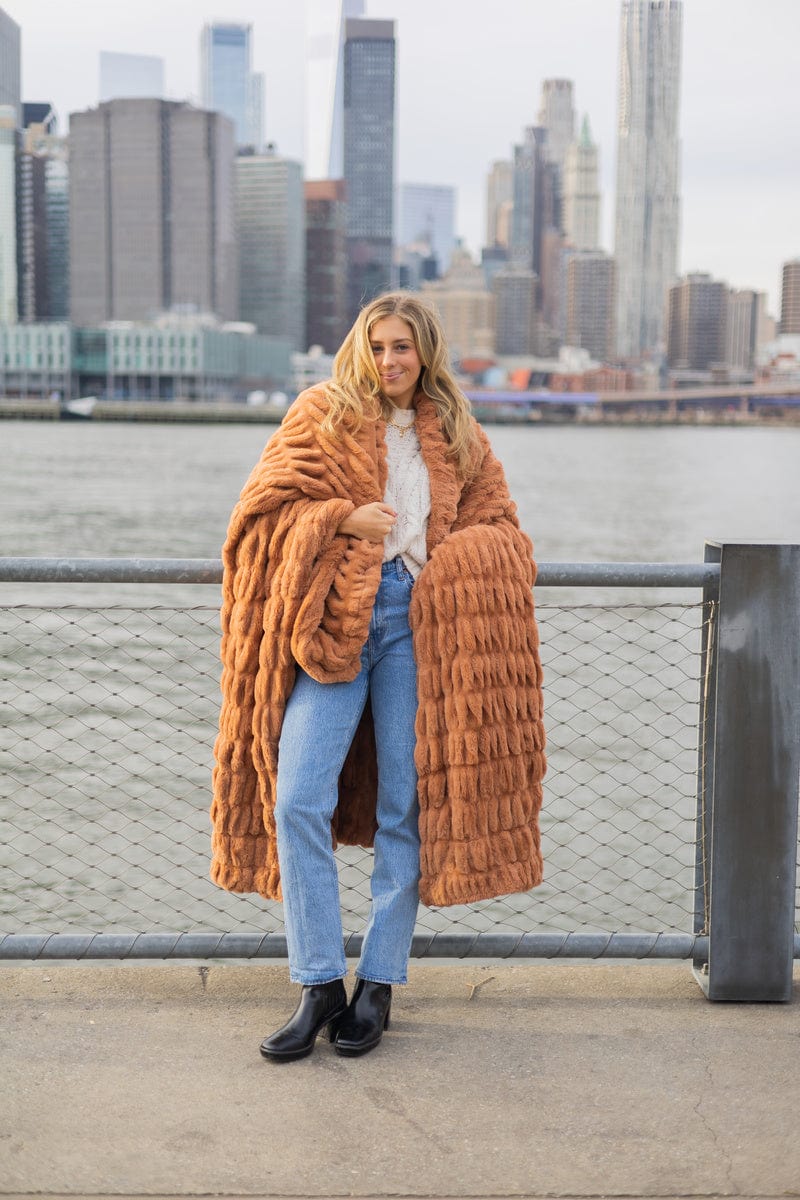 Young woman standing in front of a City skyline wrapped up in a ruched copper colored blanket.