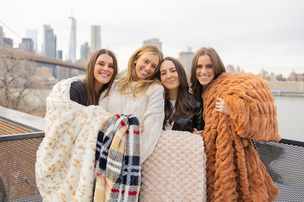 Four young women each holding a different neutral patterned blanket.