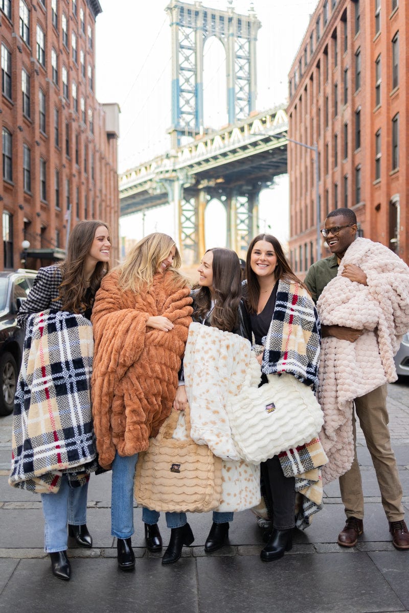 Five young adults in a city street holding various minky couture blankets and bags. 