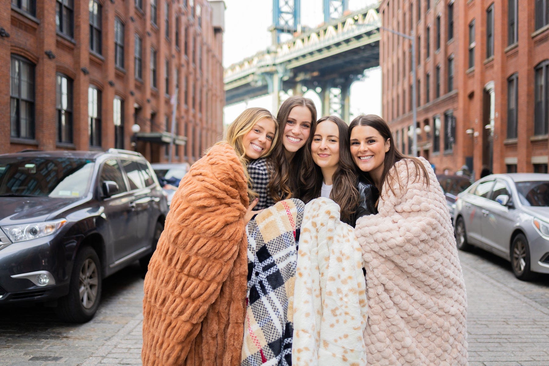 Four women standing in a city street wrapped up in various tan minky couture blankets. 