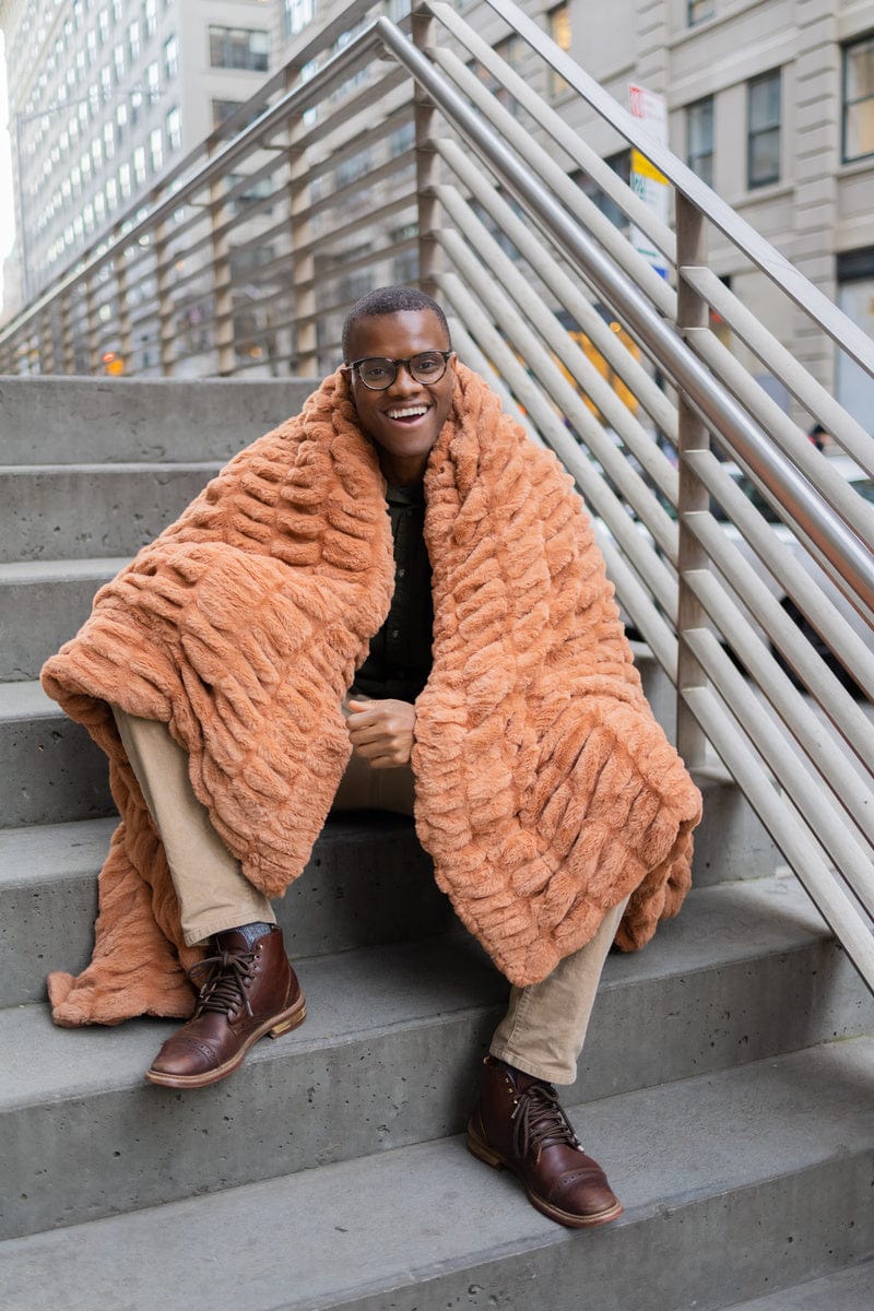 Man sitting on concrete stairs with a copper colored plush blanket around his shoulders.