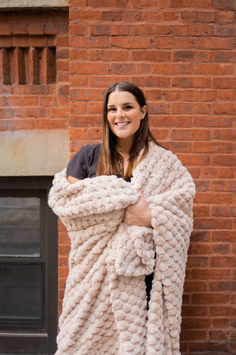 Young woman wrapped up in a light tan waffle textured blanket.