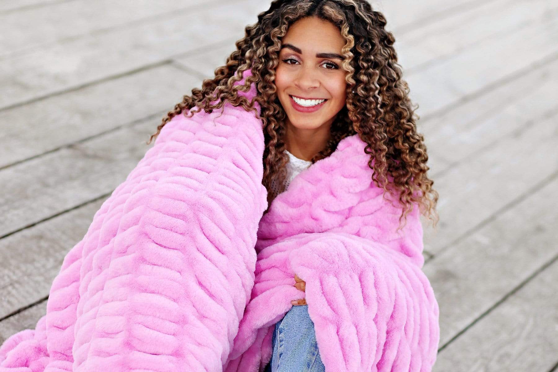 Young woman sitting wrapped up in bubble gum pink stretchy hugs collection blanket by Minky Couture.