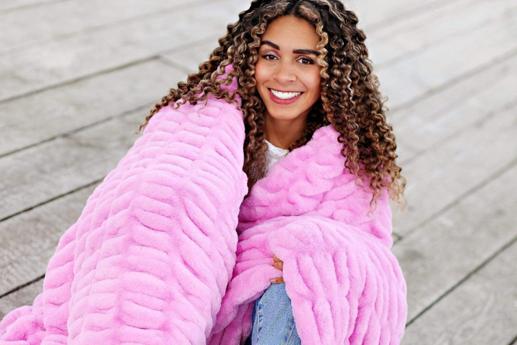 Young woman sitting wrapped up in bubble gum pink stretchy hugs collection blanket by Minky Couture.