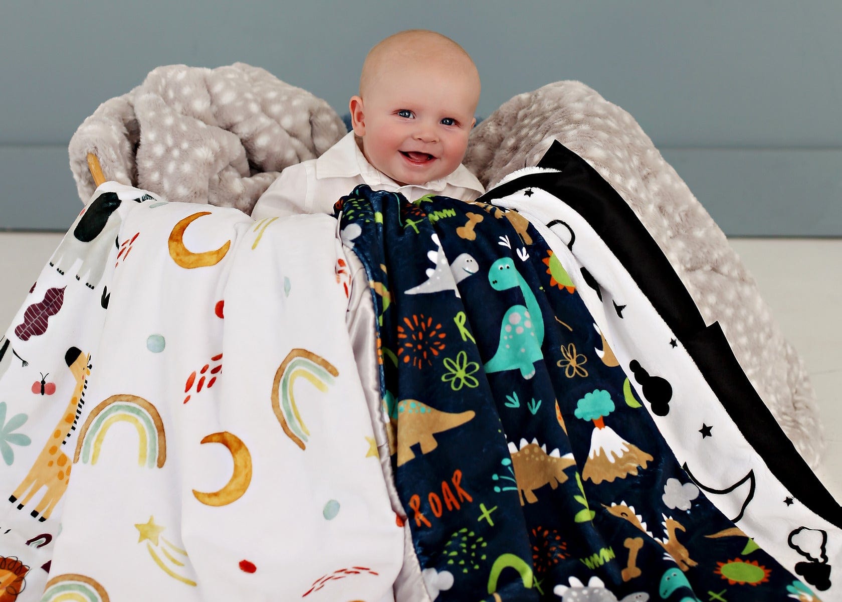 Baby boy sitting in a basket overflowing with various baby boy patterned blankets. 