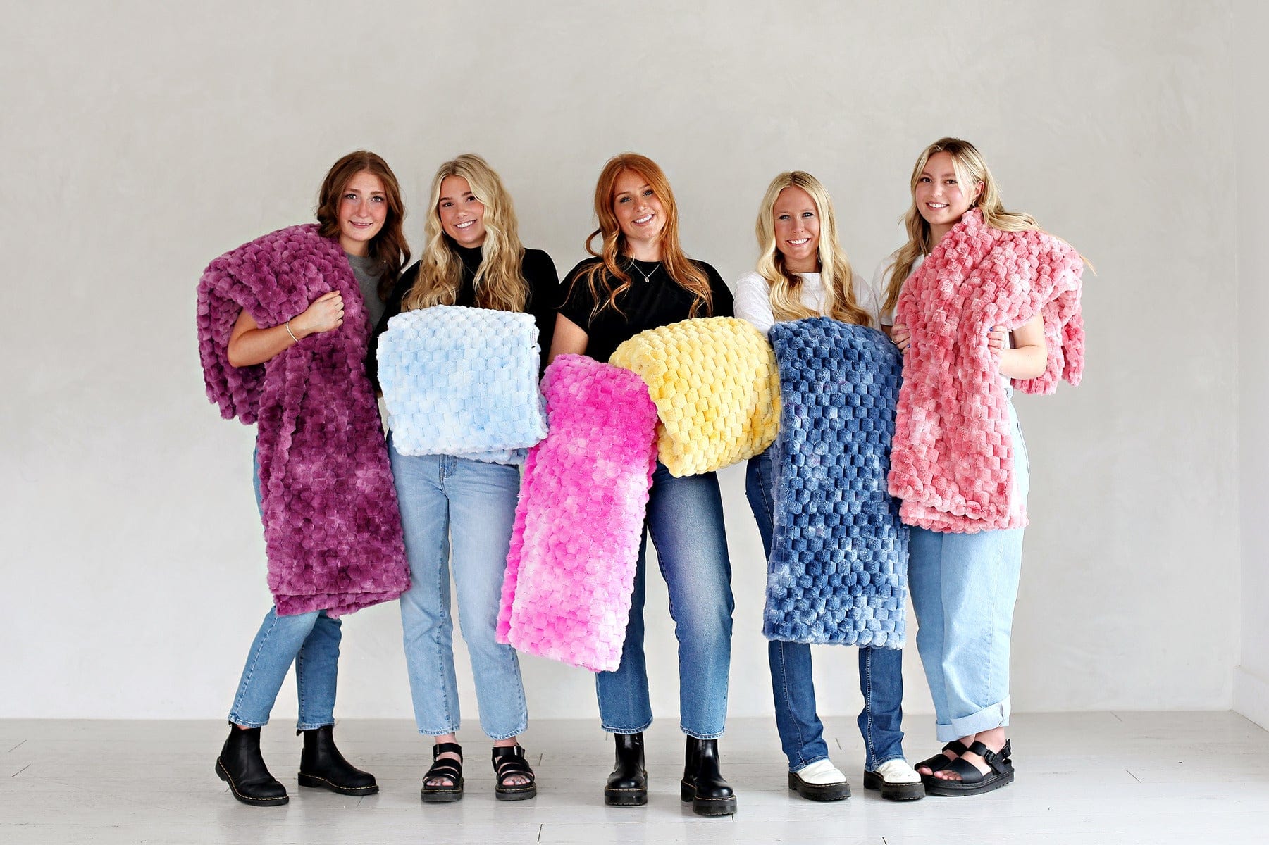 Five young women standing in a line each holding a brightly colored waffle patterned blanket.