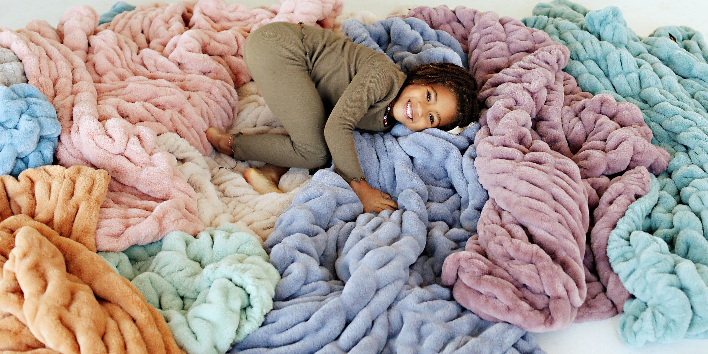 Little girl laying in a pile of different colored Minky Couture blankets 