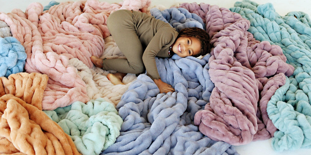 Little girl laying in a pile of different colored Minky Couture blankets 