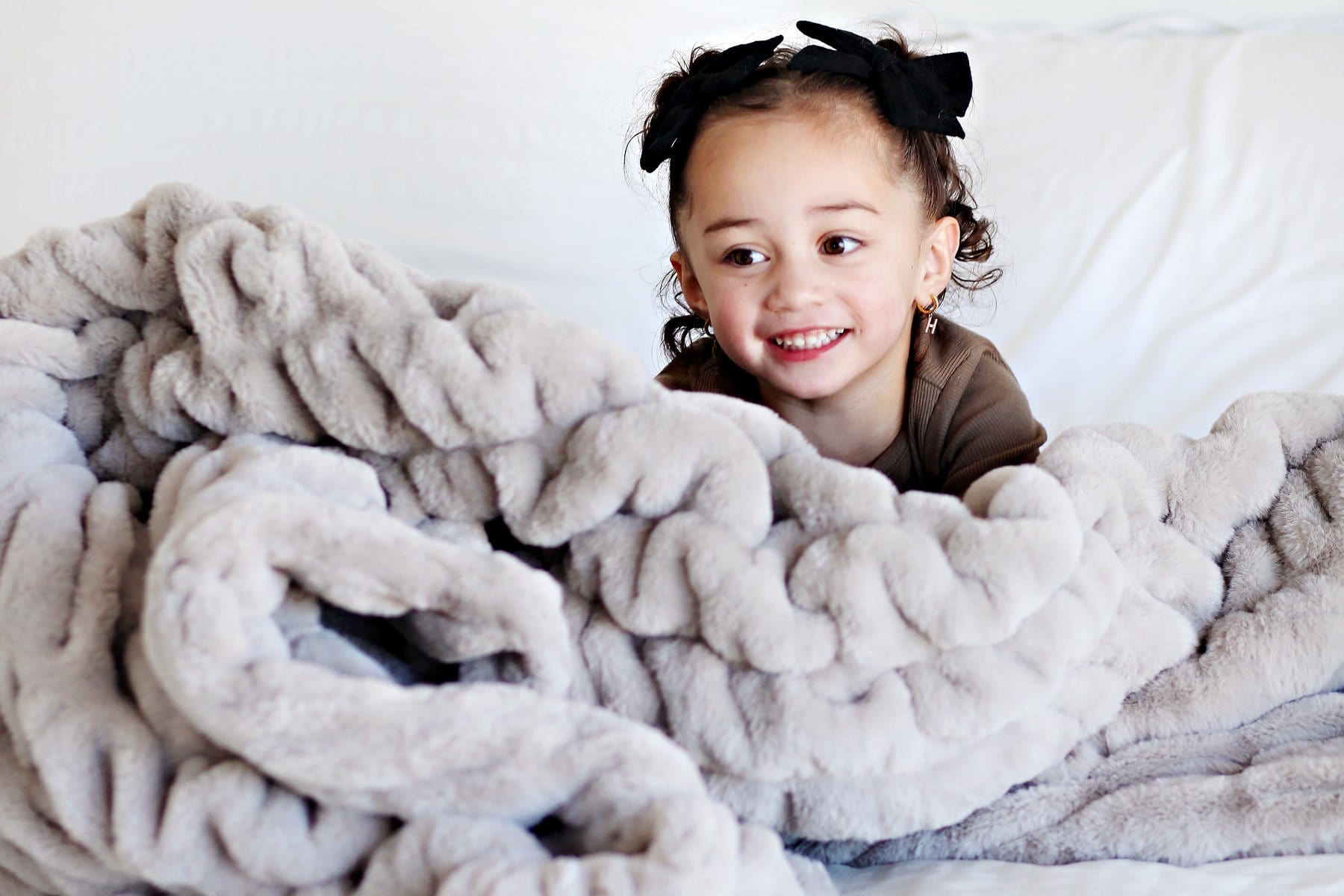 Little girl sitting under a light gray blanket.