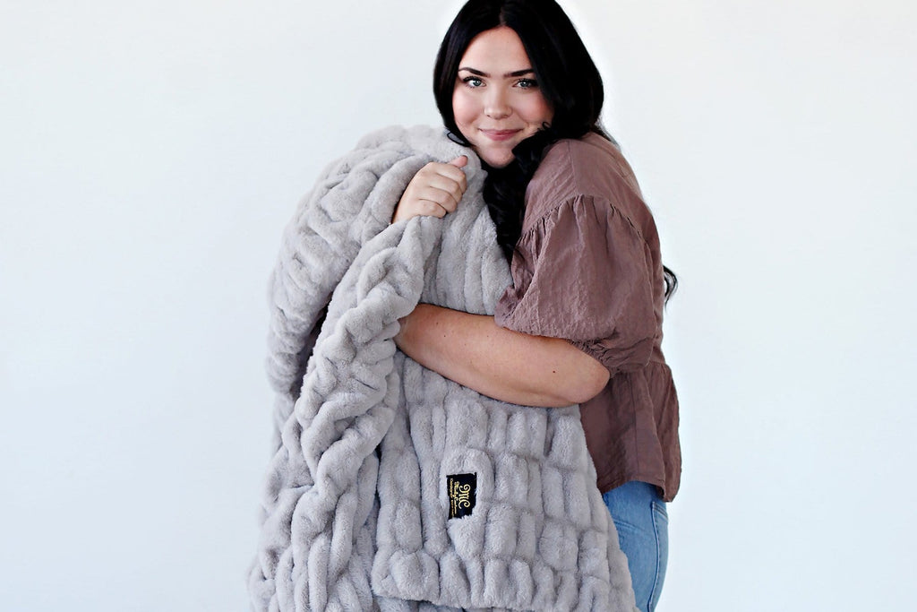 Young woman holding a light gray blanket.