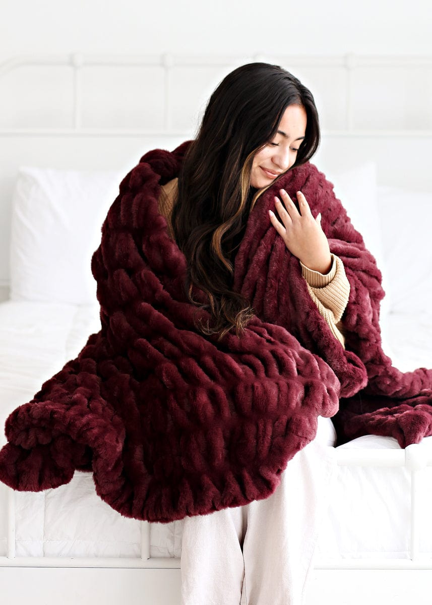 Young women sitting on a white bed wrapped up in a deep red colored stretchy blanket.