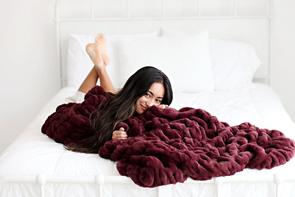 Young women laying on a white bed wrapped up in a deep red colored stretchy blanket.