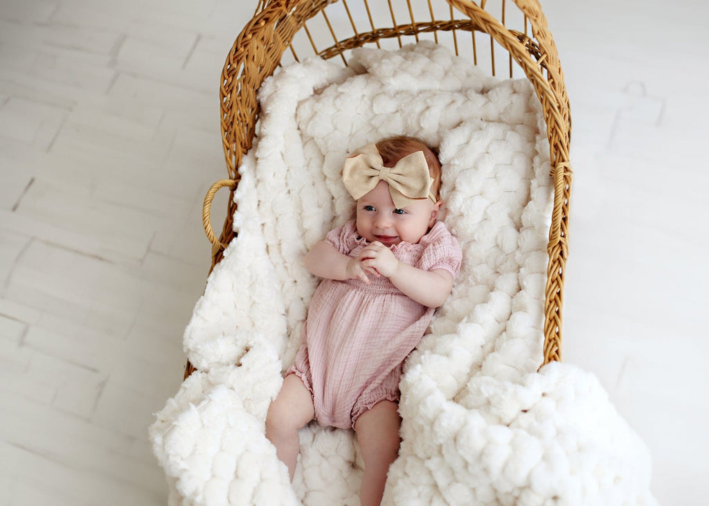 Baby girl laying in a bassinet lined with a cream waffle textured blanket.