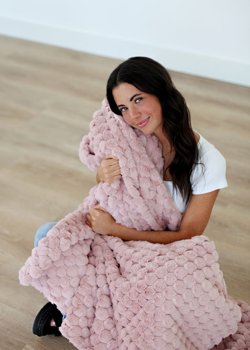 Young women sitting on hardwood flooring while holding a blush colored waffle textured blanket.