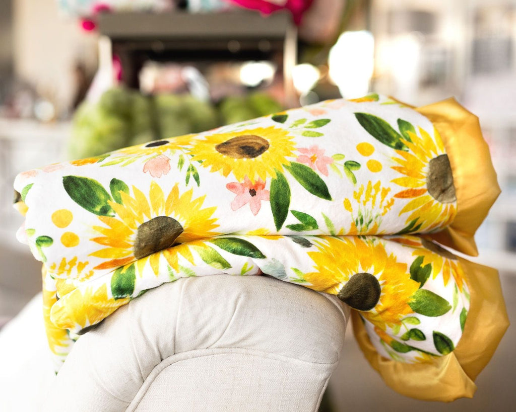 Yellow watercolor sunflower blanket folded and laid on the back of a cream chair.