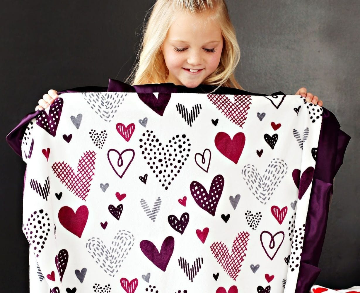 Little girl holding up Love Note Plum blanket from Minky Couture