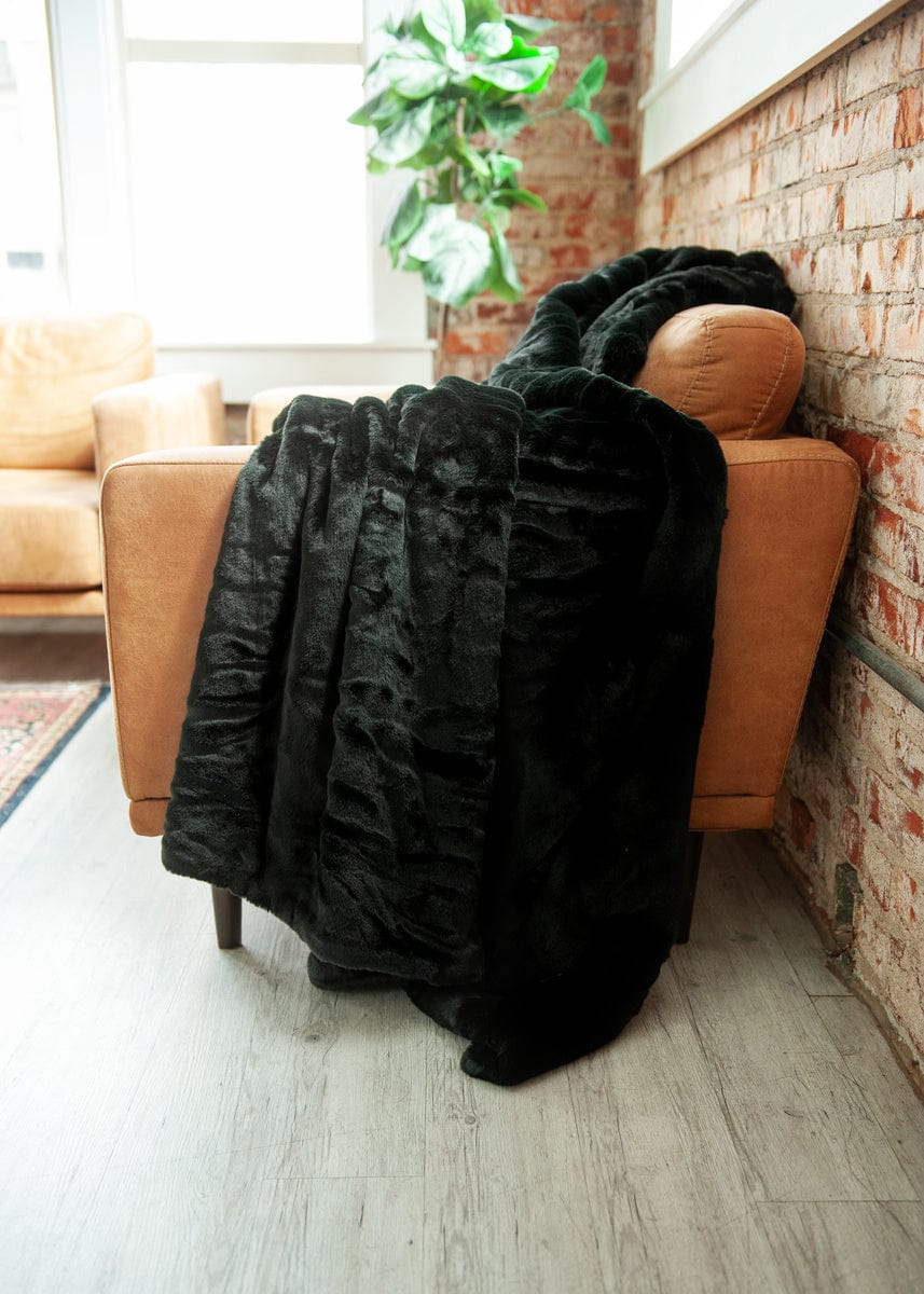 A thick black plush blanket draped over a brown leather couch.