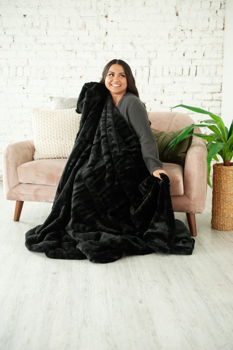 Young woman sitting on a couch holding a thick black plush blanket.