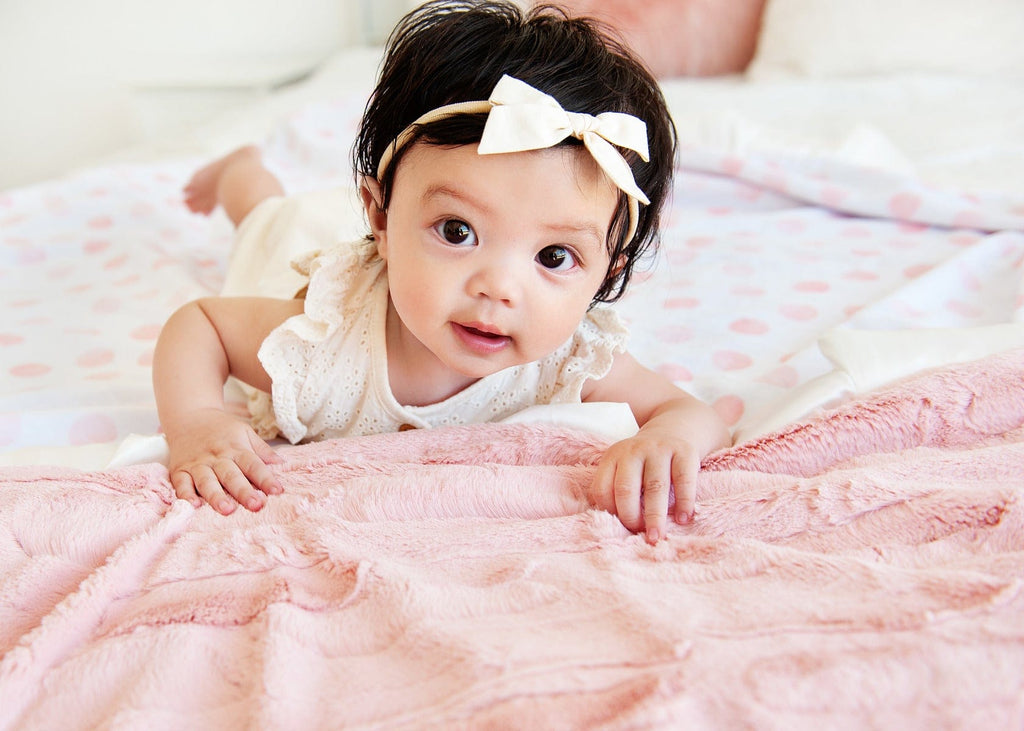Baby girl laying on a white minky blanket with pink watercolor polka dots.