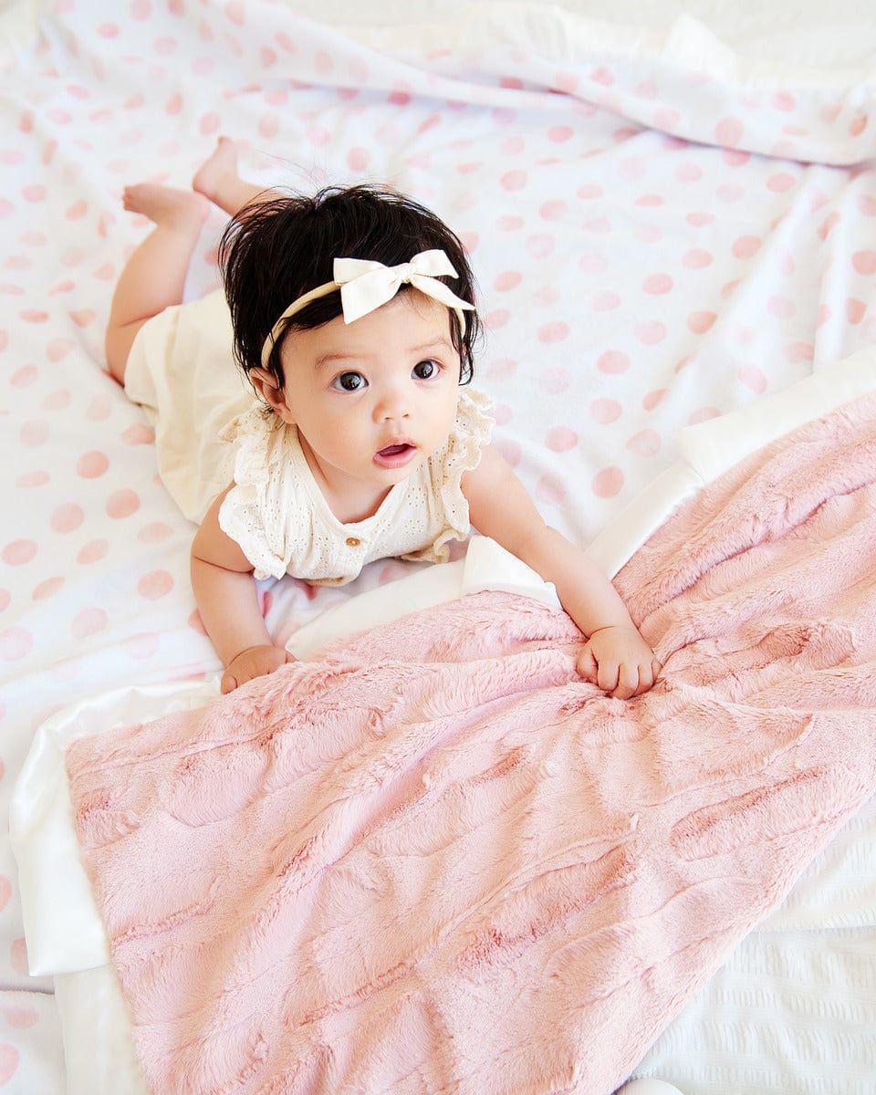 Baby girl laying on a white minky blanket with pink watercolor polka dots. 